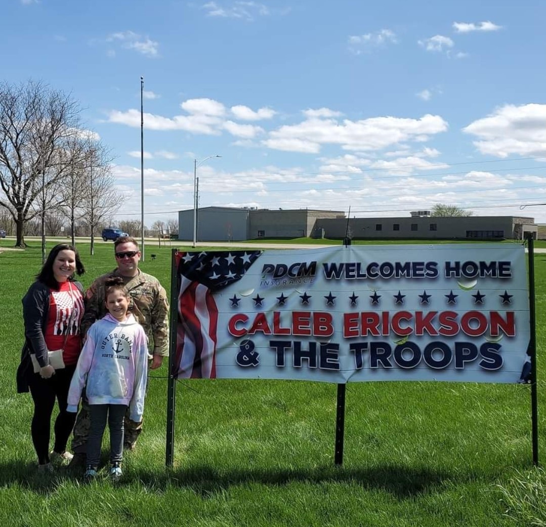 Nicole, Caleb and Cameron Erickson stand in front of 'Welcome Home' sign on PDCM lawn.